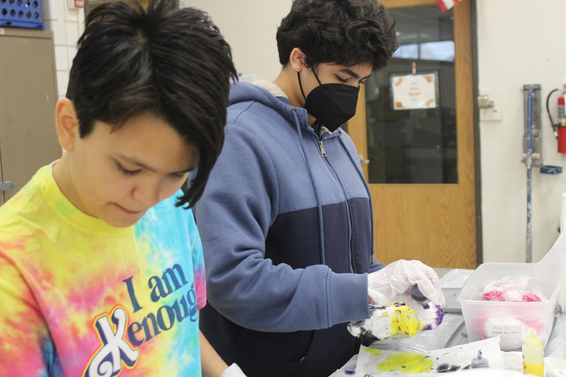 Two teenagers adding dye to t-shirts