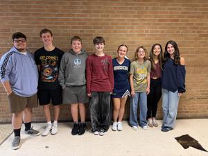 eight students standing in hallway smiling at camera