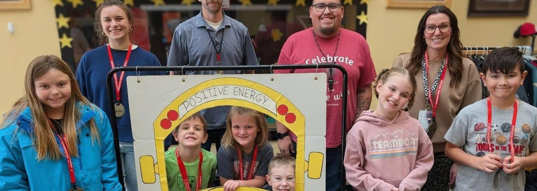 Kids posing joyfully in front of a bus backdrop with medals.