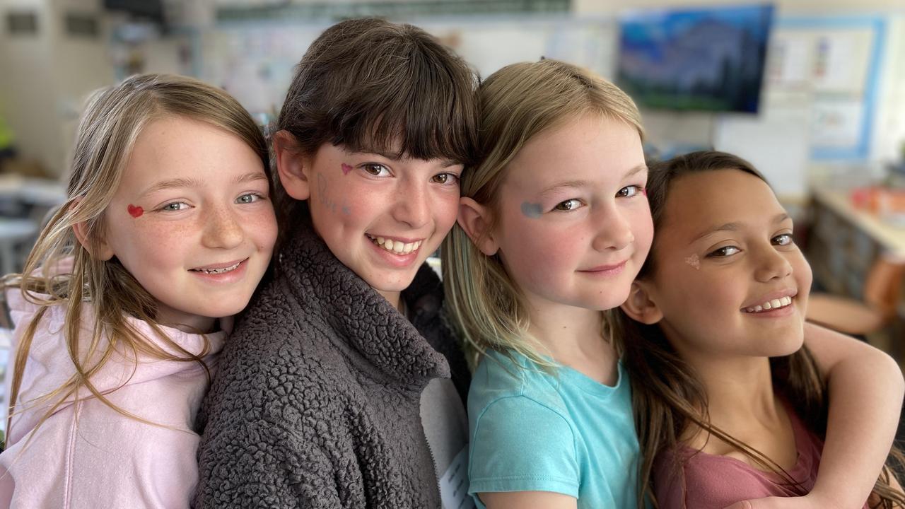 Four smiling girls posing together, each with colorful face paint.