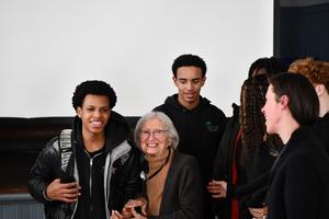 Magda Bader holds the hand of a PROMISE student while others stand nearby after her presentation