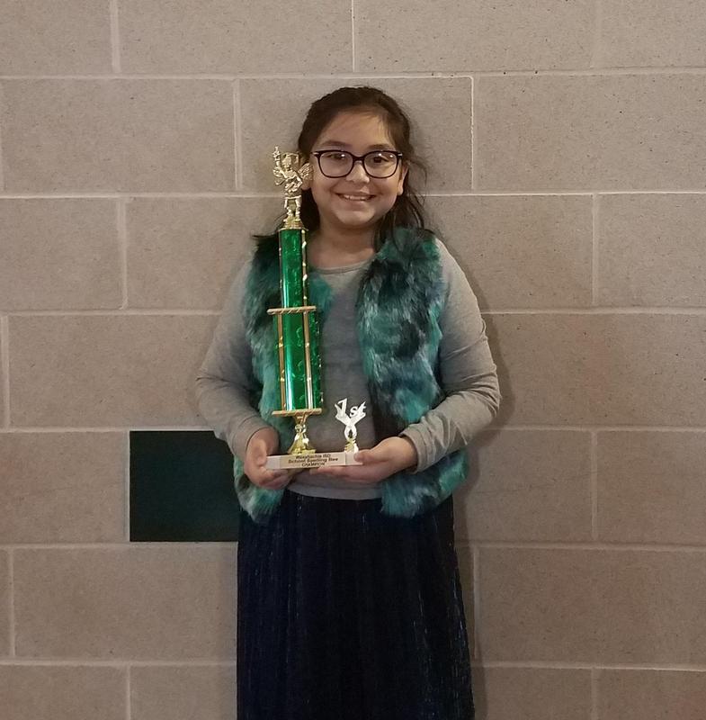 girl poses with the trophy she earned as the spelling bee champion