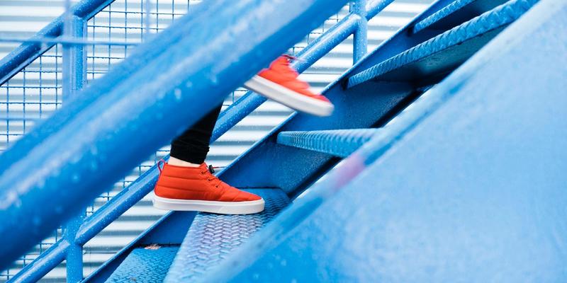 A person walking up blue stairs wearing bright red shoes.