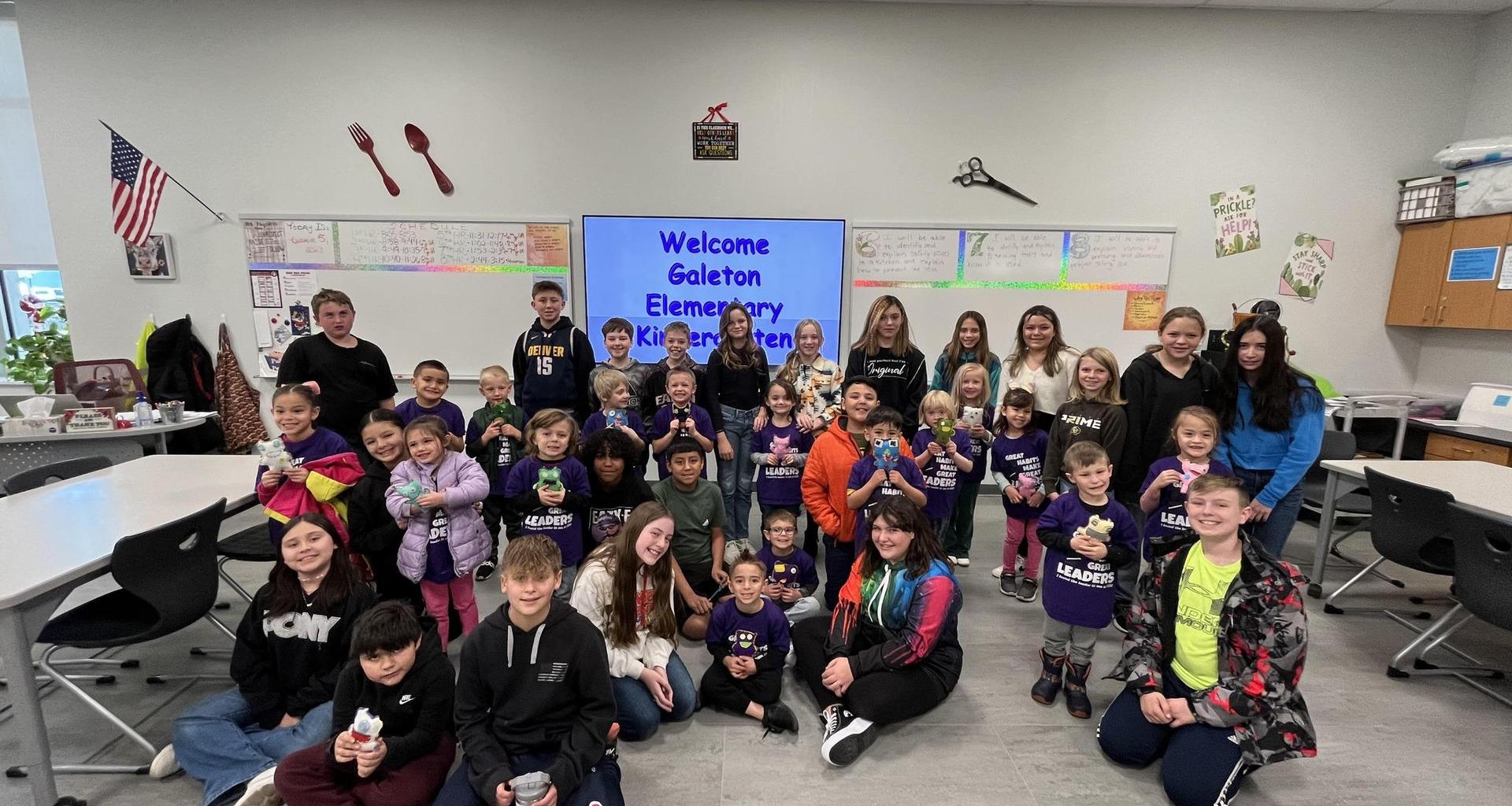 A large group of students and teachers gathered in a classroom, holding snacks and smiling.