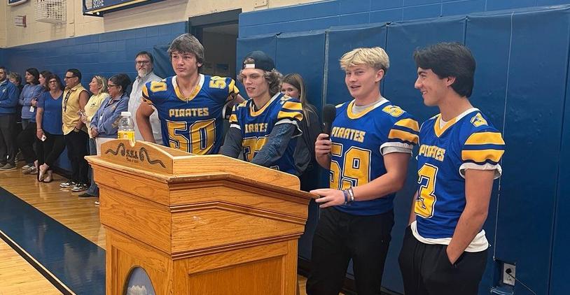 Four football players wearing blue and gold jerseys stand at a podium during an event.