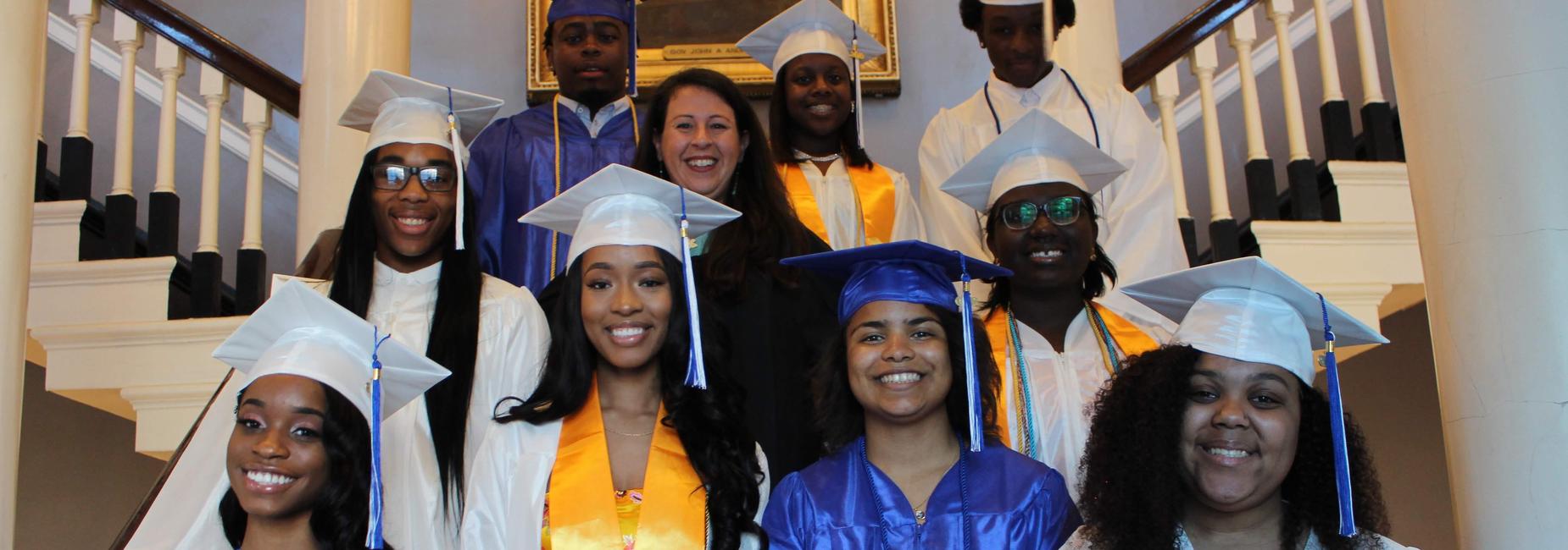 Students stand with a teacher at their graduation.