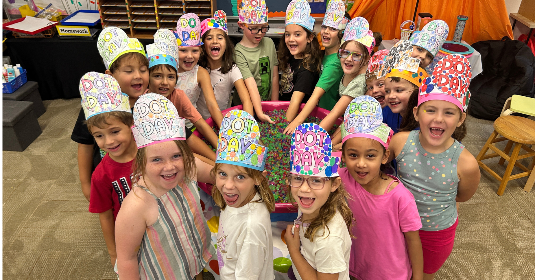 Children wearing colorful hats celebrating Dot Day with smiles around a table.