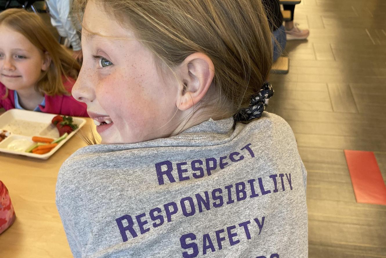 Child smiling and showing a shirt with values: respect, responsibility, safety.