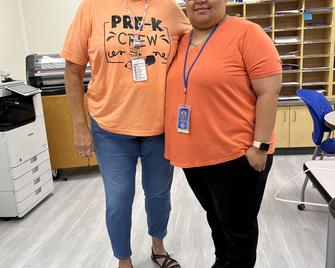 Two women standing together in orange shirts, smiling for the camera.