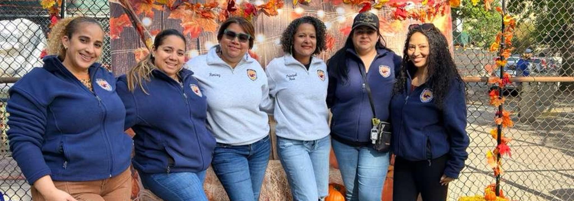 Group of six women posing together at a festive outdoor setting.