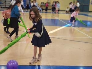 A girl uses an umbrella to push a balloon.