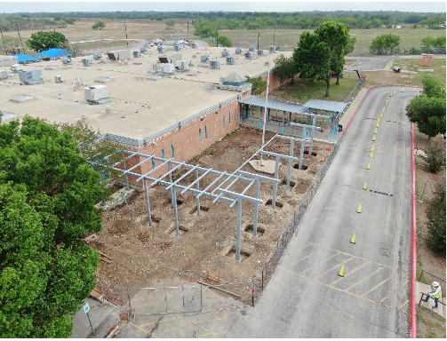 Aerial view of a school construction site with steel beams and cleared ground.
