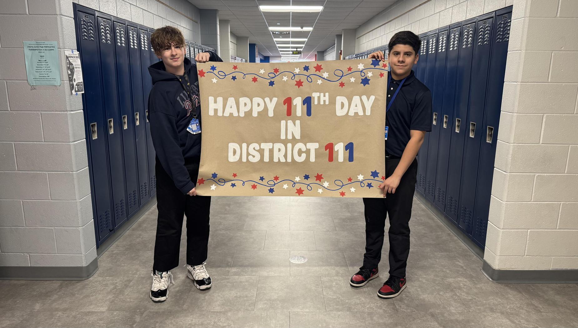 Two students holding a large celebratory sign in a school hallway.