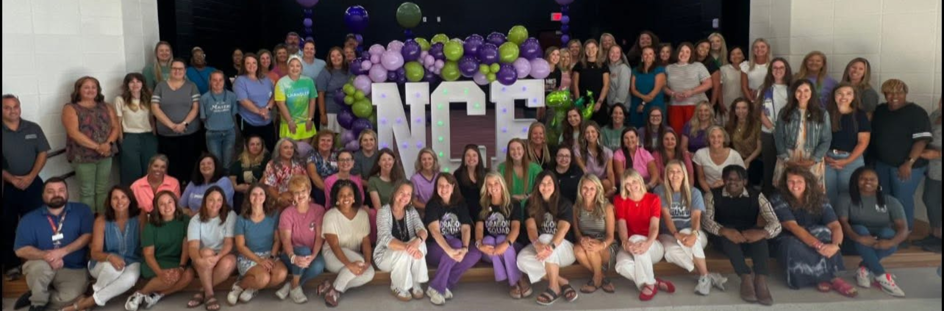Group photo of staff members in front of a colorful balloon display with 'NCE' letters.