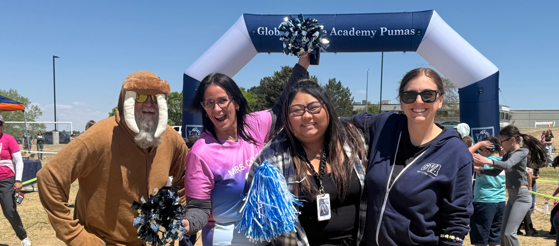 Four people celebrating at a school event under a large archway.