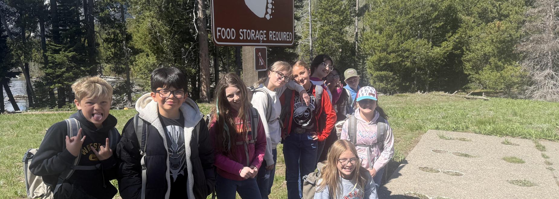 Group of kids posing near a food storage sign in a park.