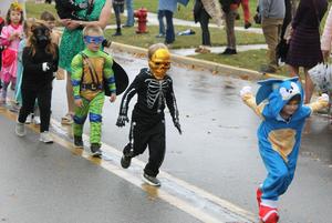 Children in costumes parade along a street on a rainy day.