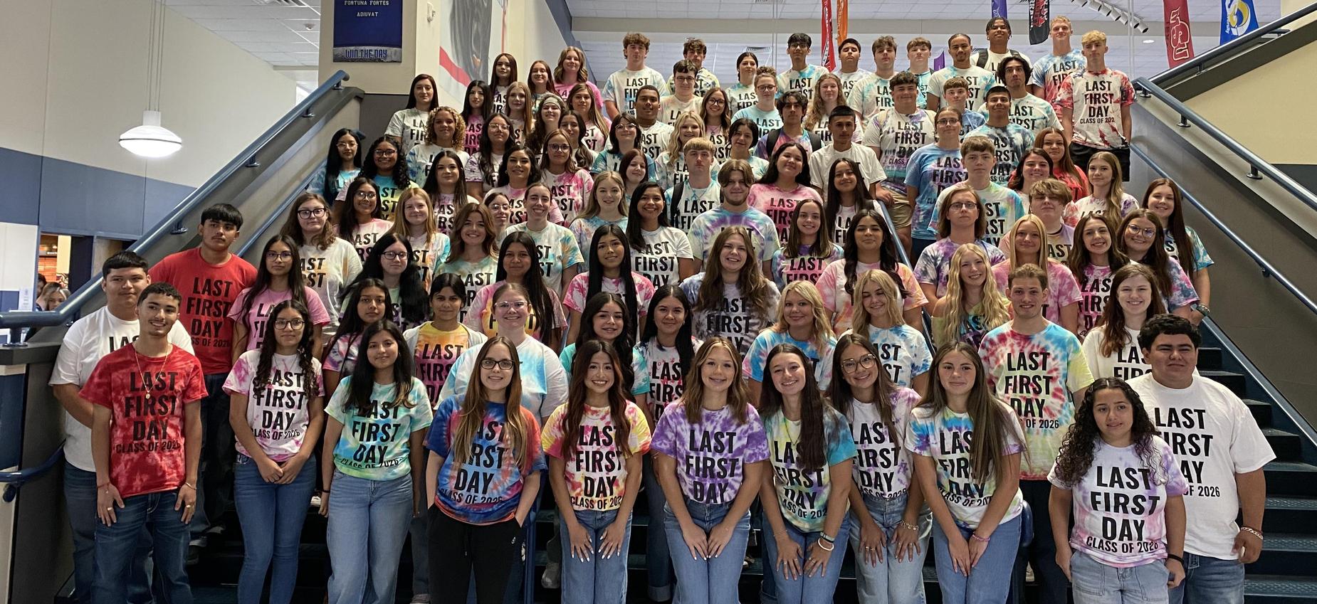 A large group of students wearing colorful tie-dye shirts pose together in a school setting.