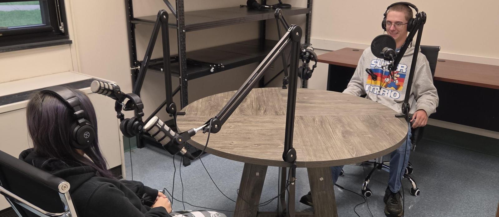 The Dragon Den podcast, two students sitting at a table with headsets and microphones.