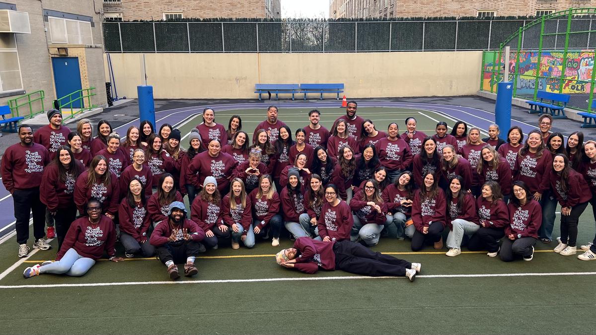 A large group of diverse individuals wearing maroon sweatshirts, posing together on a sports court.