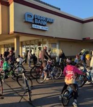 A group of people with bicycles gathered in front of Parkway Bank.