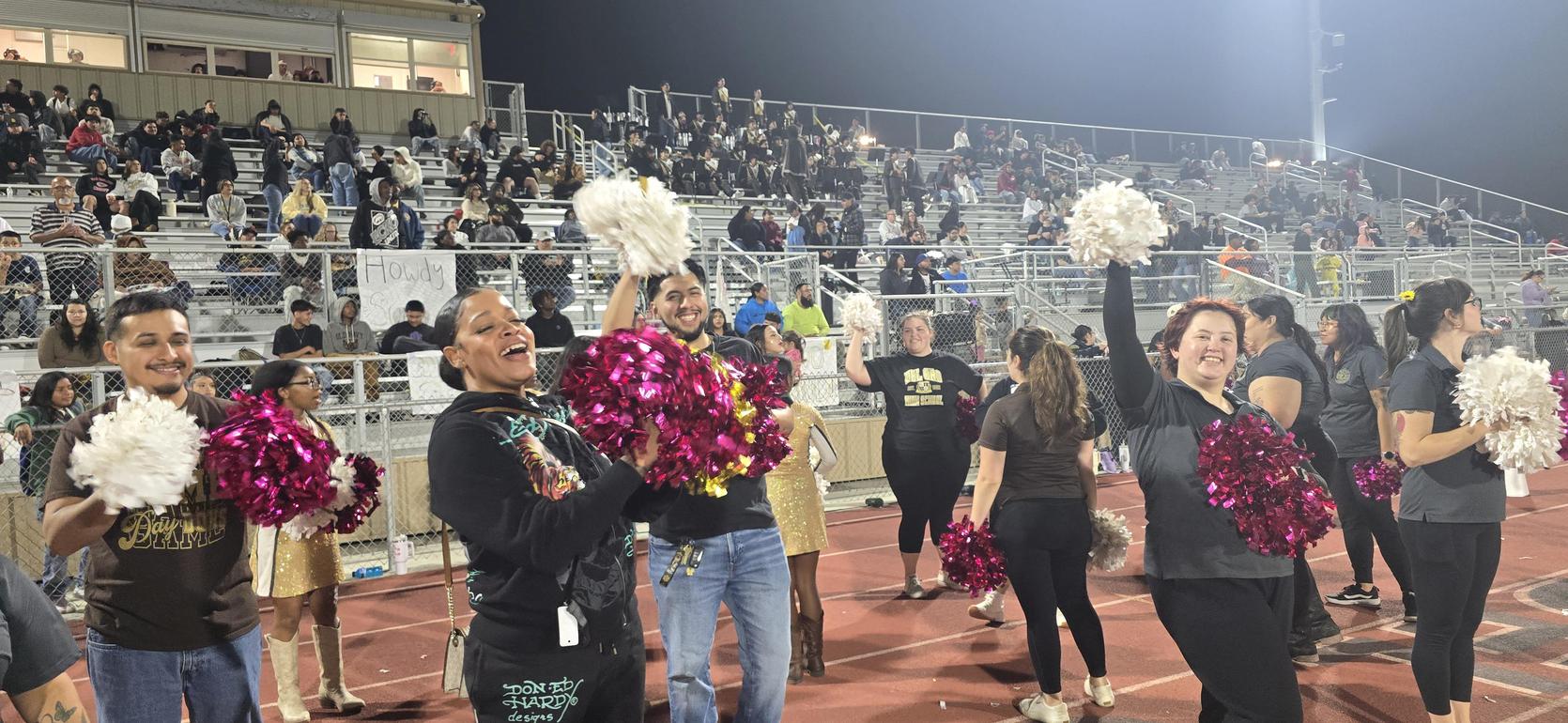 Cheerleaders wearing colorful pom-poms perform in front of a cheering crowd.