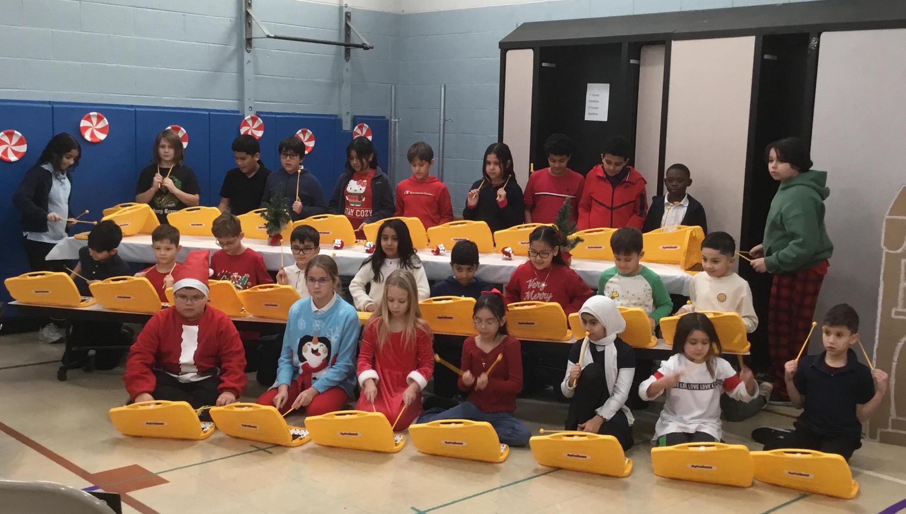 A group of children sitting at yellow keyboards, performing together in festive attire.