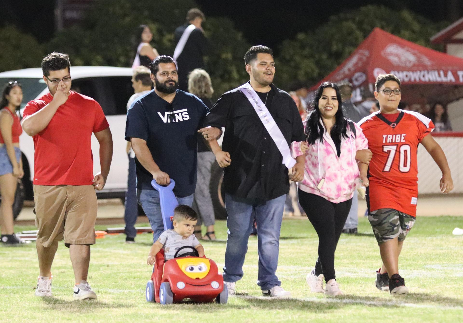 homecoming king and queen candidates walking across the field with their escorts