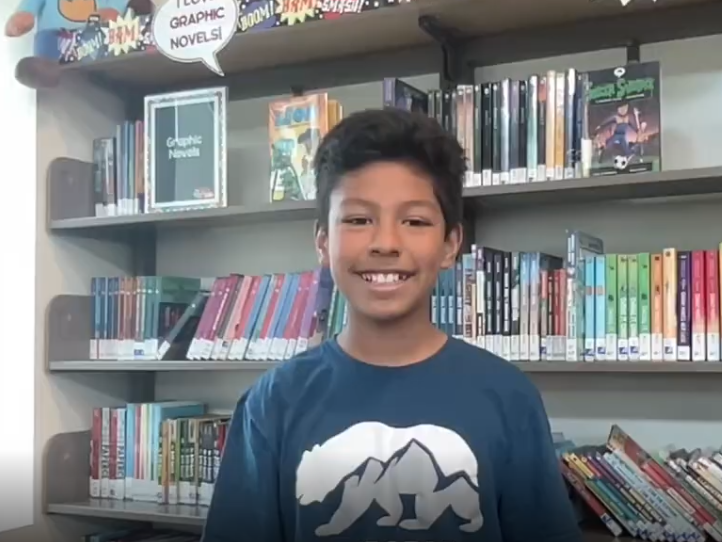 5th grader Mateo stands in front of a bookshelf with colorful books