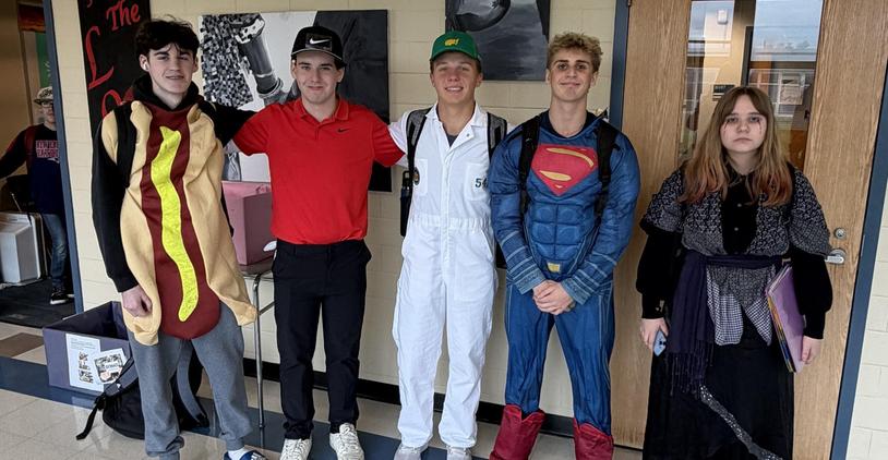 Five students in costumes, including a hot dog and Superman, standing together in a hallway.
