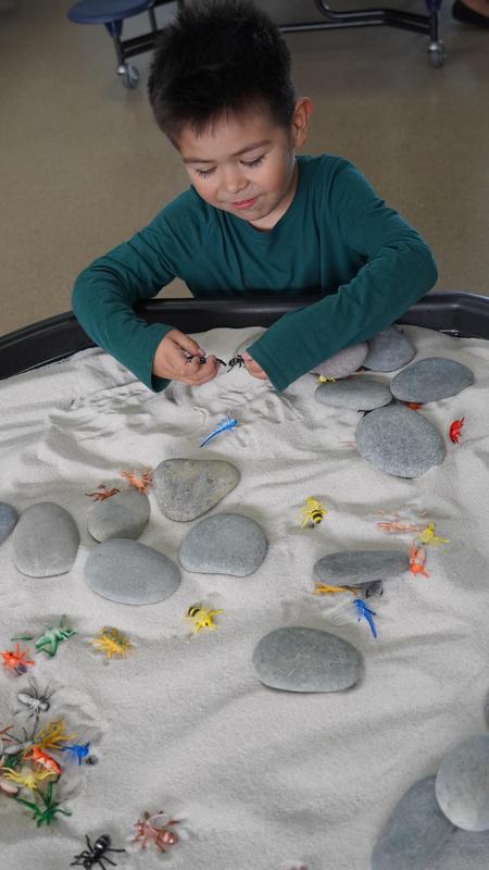 Child playing in sandbox with sensory toys