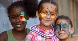 Three children smiling with butterfly face paint outdoors.