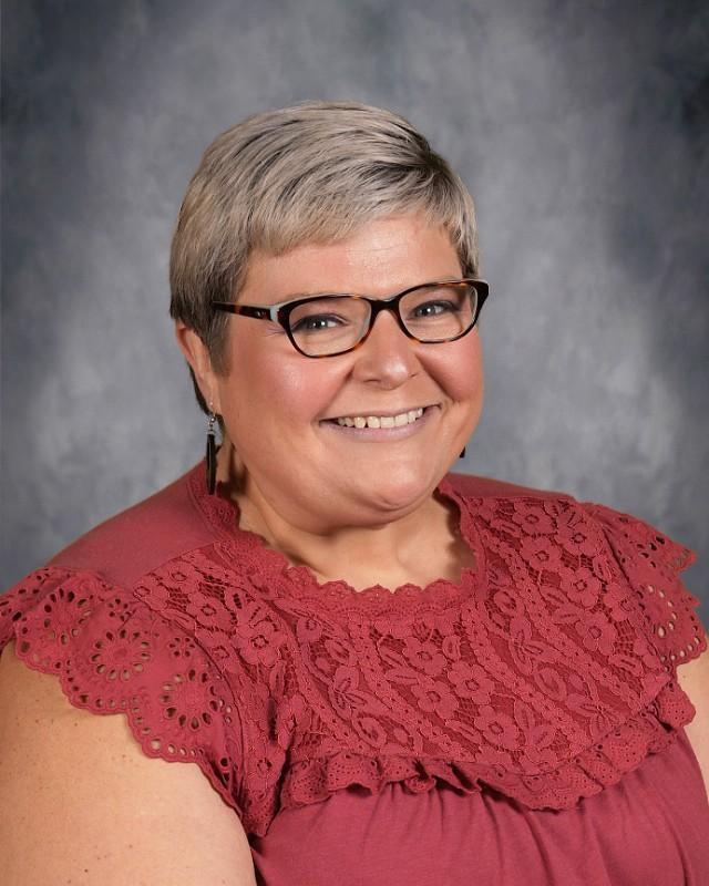 Woman with short purple hair and glasses smiling warmly.