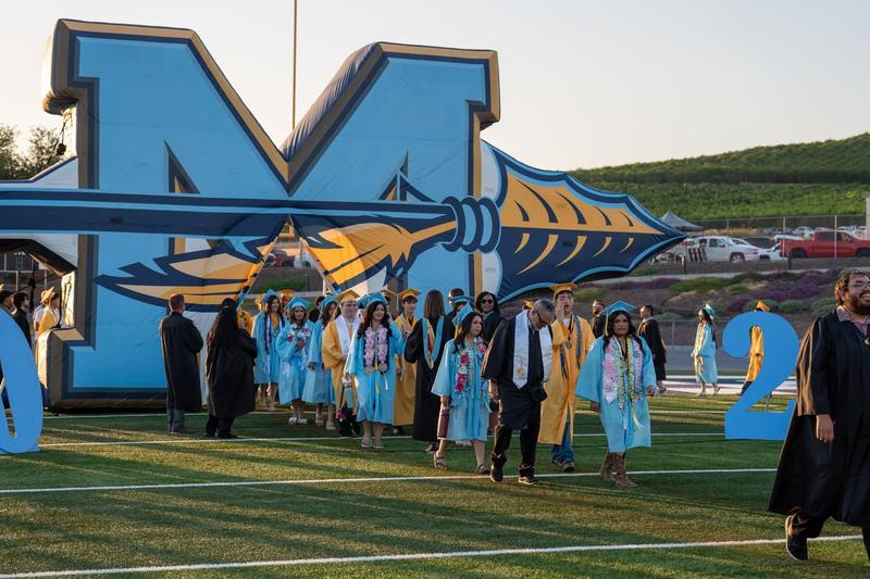 MHS Graduates enter graduation under the M logo
