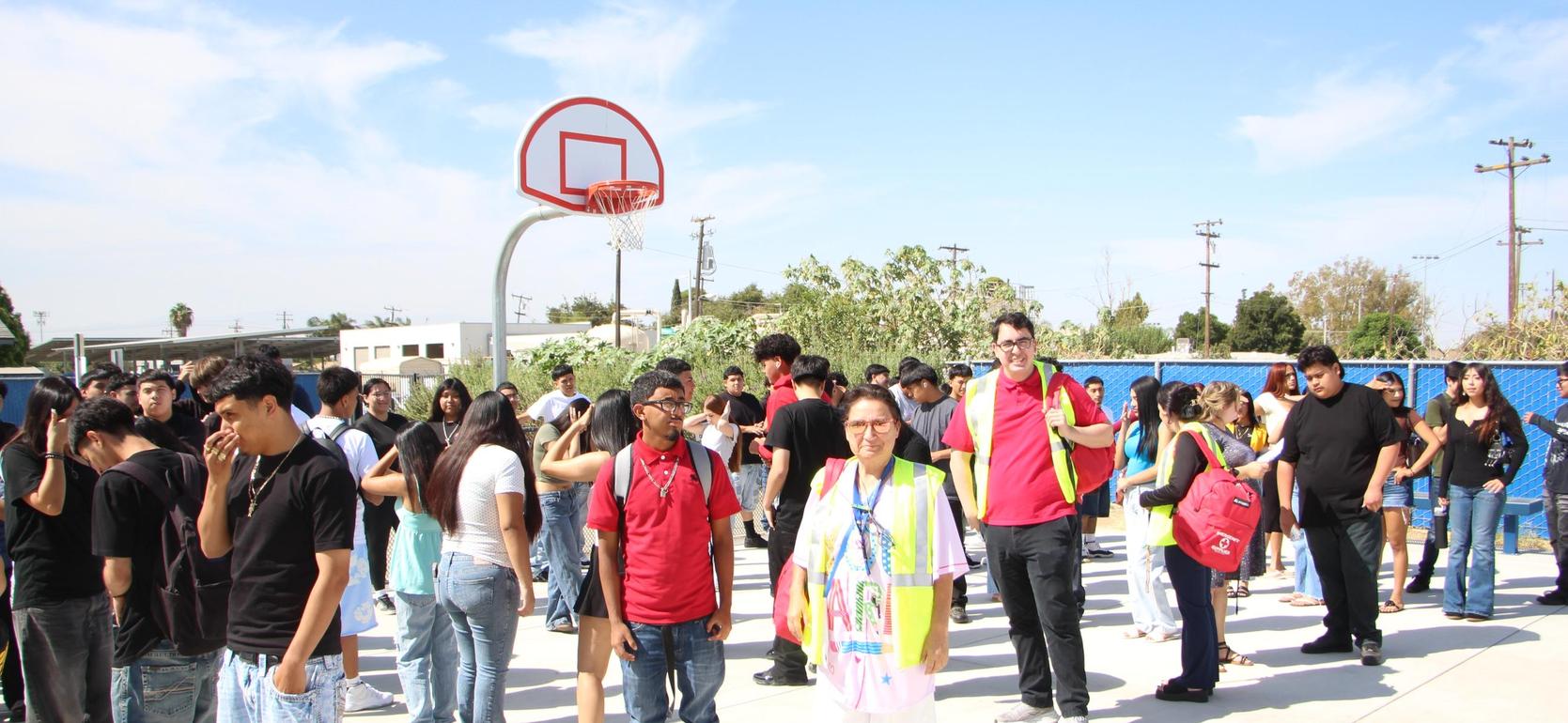 A group of people waiting in a line outdoors near a basketball hoop.
