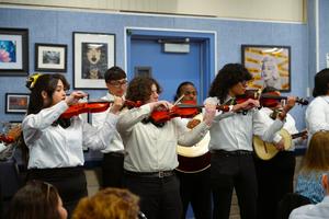 A group of students from Santa Fe High School’s Mariachi Band play their violins inside a full district board room, while dressed in traditional mariachi attire.