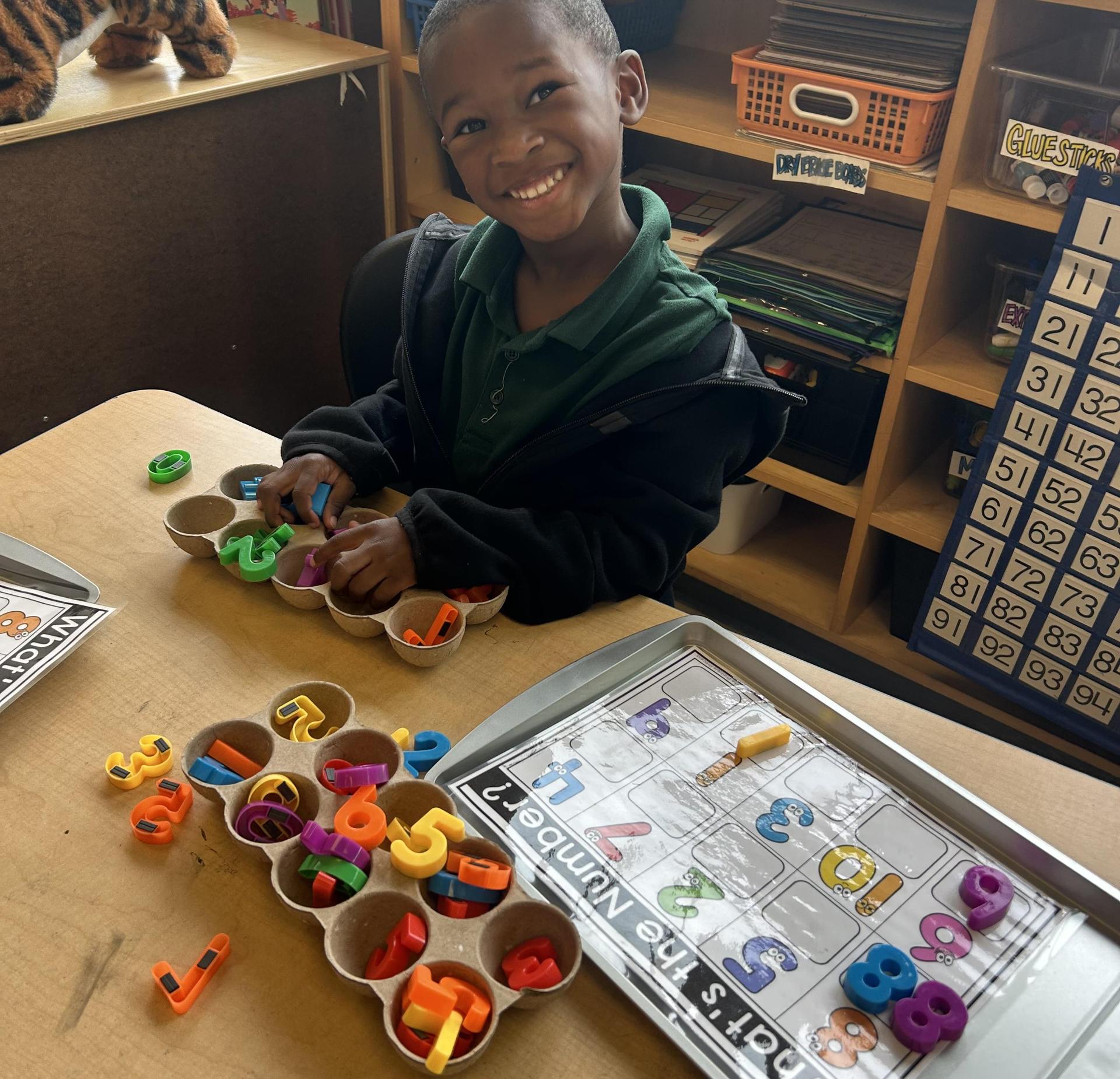A young boy smiles while playing with colorful magnetic numbers at a table.