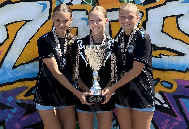 Three female soccer players holding a championship trophy