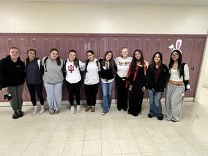 A group of twelve students dressed in various costumes pose together in front of lockers.