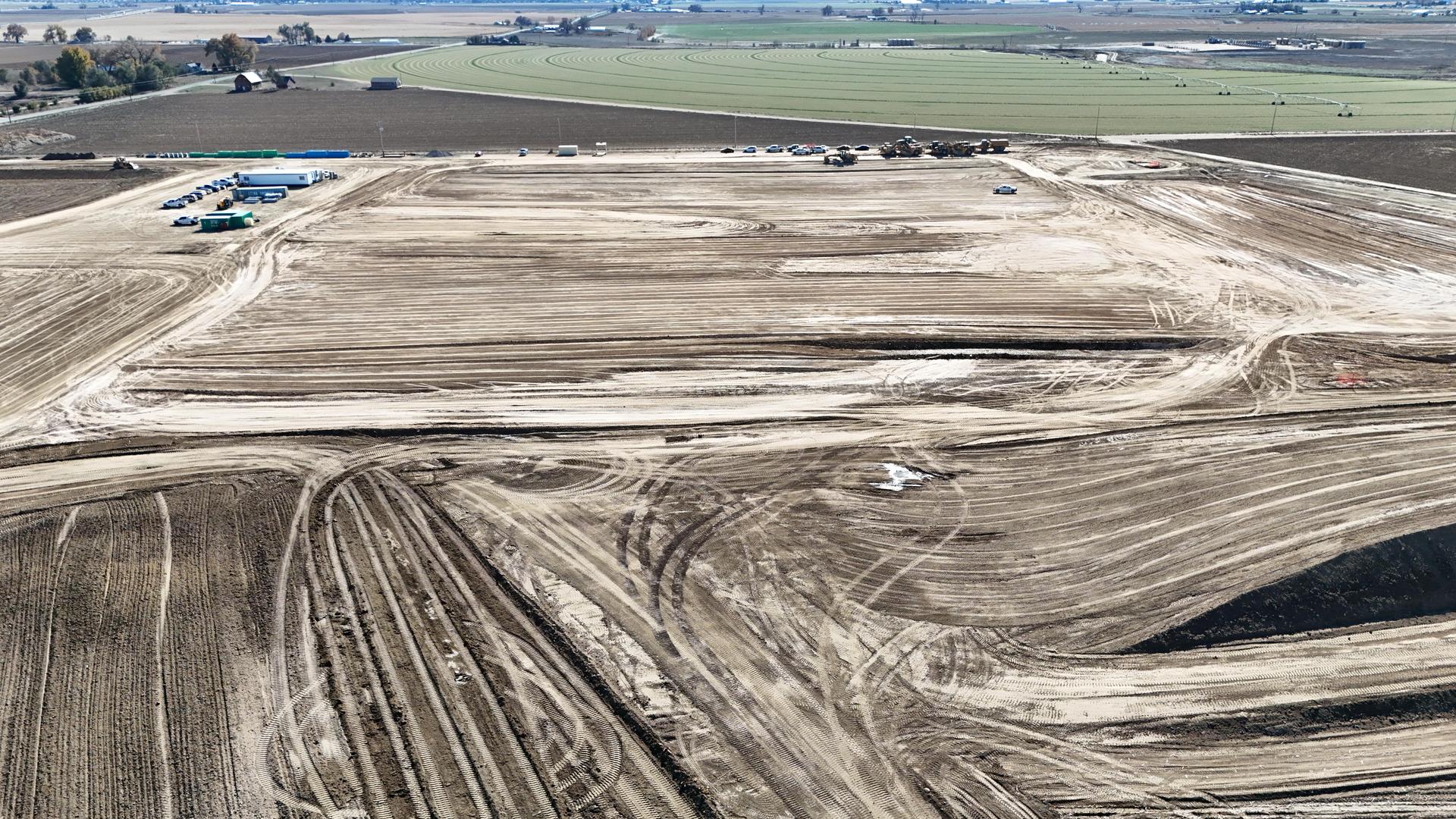 Aerial view of a large open field with construction vehicles and equipment in different areas.