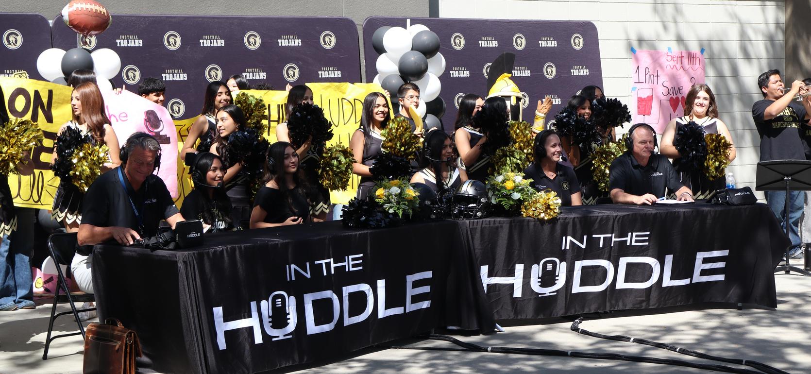 Cheerleaders and broadcasters at a sports event, with banners and decorations.