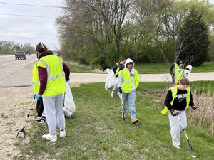 Group of volunteers picking up trash along a roadside, wearing bright vests.