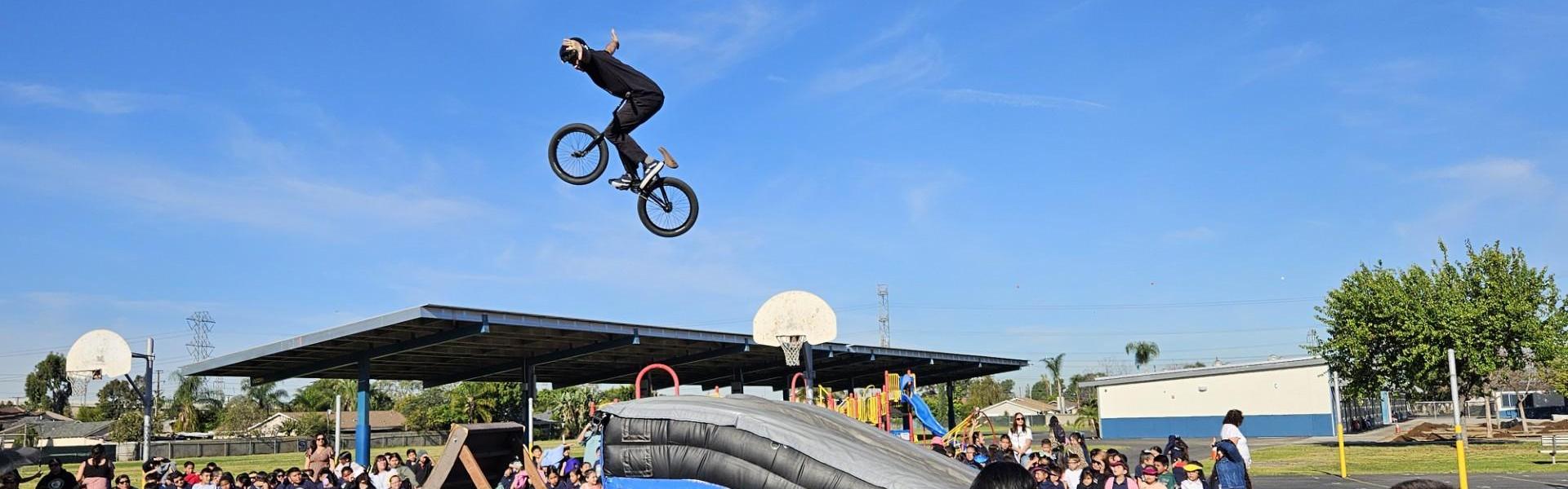 BMX rider performing a jump over a crowd at a school event.