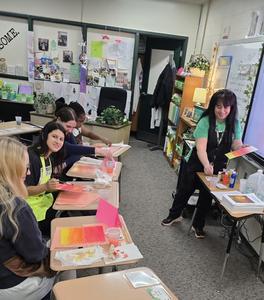 A teacher demonstrates painting techniques to students in a classroom.