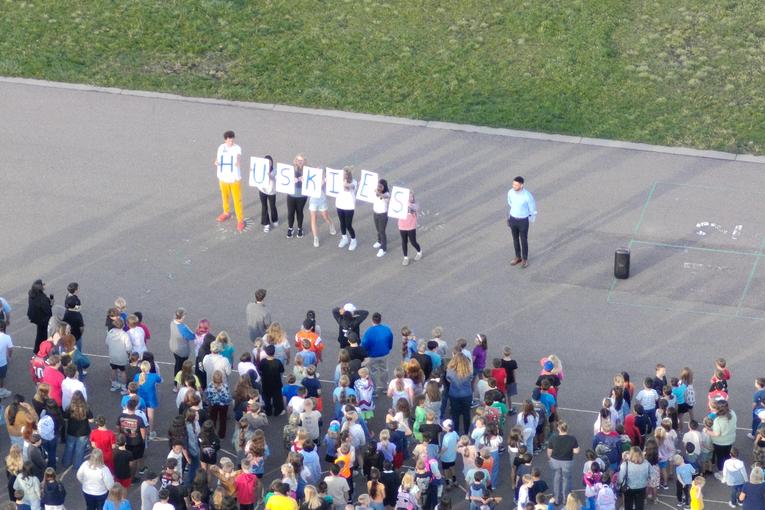 Group of people holding letters to spell 'HUSKIES' at an outdoor event.