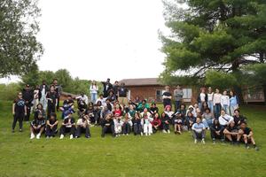 Big gathering of people sitting on grass in front of a building, outdoors.