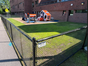A fenced-in playground with a play structure and a grassy area.