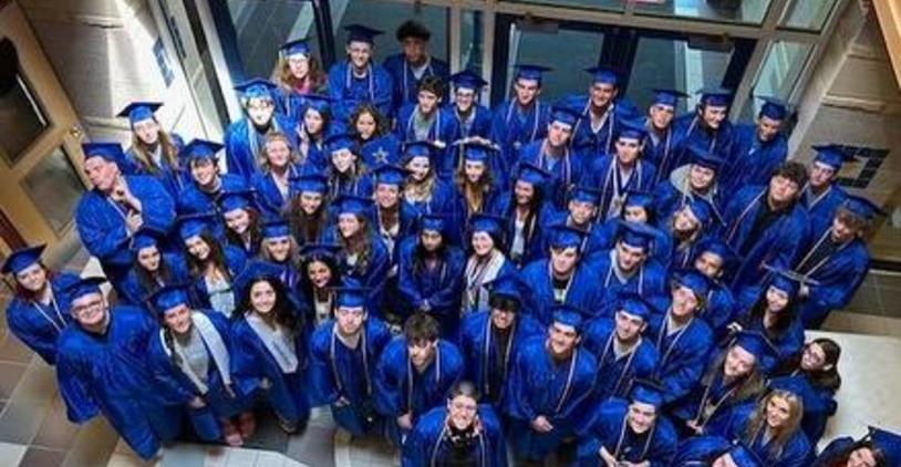 Large group of graduating students wearing blue caps and gowns posing indoors.