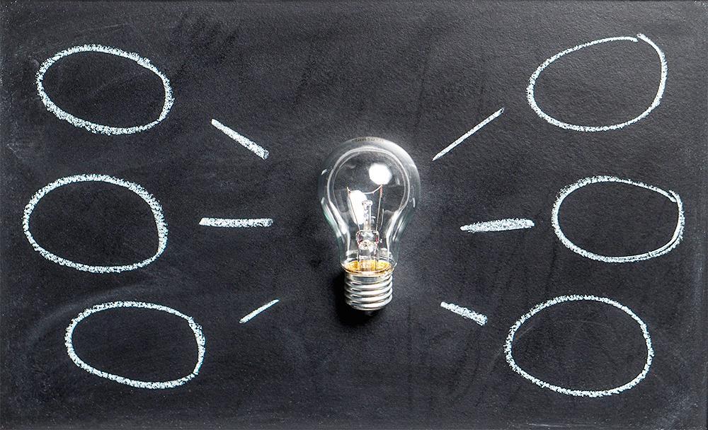 A lightbulb against a black chalkboard, with thought bubbles on both sides