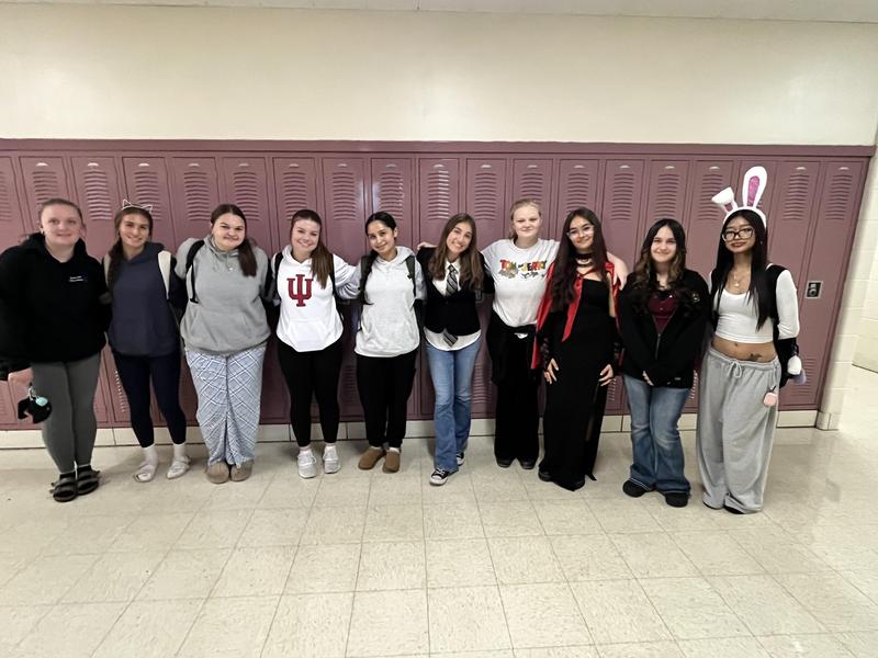 A group of twelve students dressed in various costumes pose together in front of lockers.